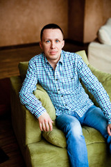 Man in shirt and jeans sitting in a chair at home