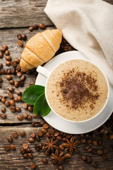 Close-up of coffee cup with roasted coffee beans on wooden background.