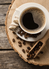 Close-up of coffee cup with roasted coffee beans on wooden background.