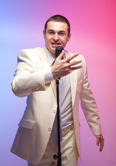 Man in white suit  with microphone. Vivid emotions. Colored back