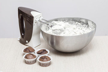 Mixer near cupcakes and a bowl with butter cream