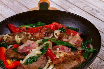 Frying pan with fried meat, bacon, red pepper and spinach