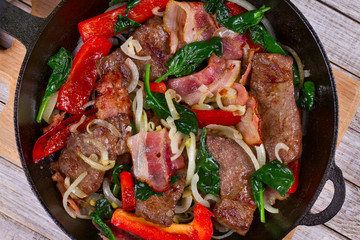 Frying pan with fried meat, bacon, red pepper and spinach