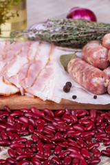 Red beans, thyme, sausages and bacon on wooden background