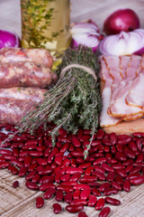 Red beans, thyme, sausages and bacon on wooden background