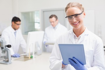 Obraz premium Smiling scientist using tablet while colleagues working behind