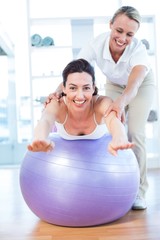 Trainer helping woman on exercise ball