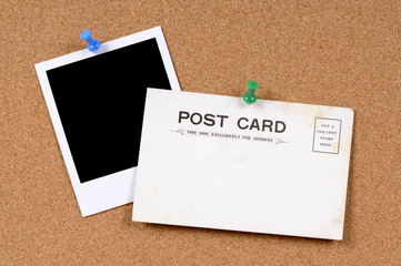 Old postcard or post card vintage retro pinned to a cork bulletin board background with one single blank polaroid style photo frame print