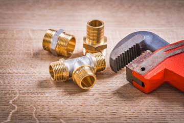 Brass Pipe Connectors And Monkey Wrench On Wooden Board