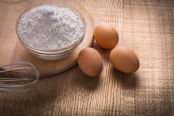 three eggs whisp and bowl with flour