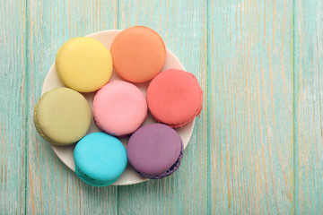 Fototapeta na wymiar Tasty colorful macaroons in small plate on color wooden background