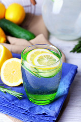 Fresh water with lemon and cucumber in glassware on napkin on wooden table, closeup