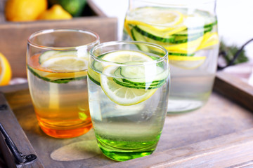 Fresh water with lemon and cucumber in glassware in wooden tray, closeup