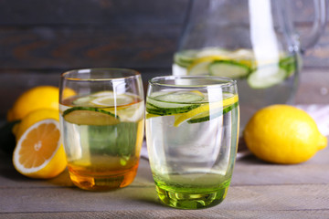 Fresh water with lemon and cucumber in glassware on wooden background