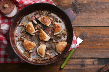 Fried dumplings with onion and bacon in frying pan,