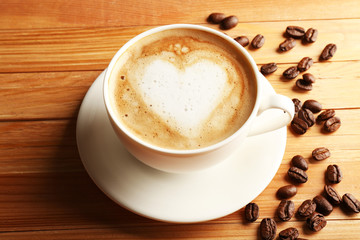 Cup of coffee latte art with grains on wooden table, closeup