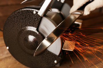 Knife sharpener and hand with blade on wooden table, closeup