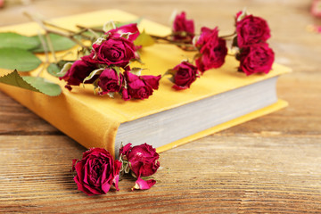 Dried roses with book on wooden table, closeup