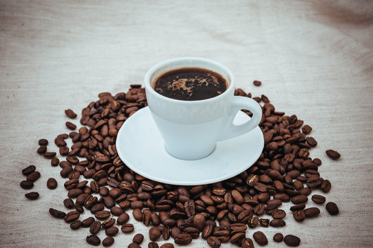 Cup of coffee and roasted beans on beige background