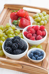 fresh berries and green grapes on a wooden tray, top view