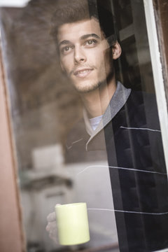 Man looking through the window with a cup of coffee in hand