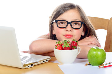 a little girl sitting at his desk with a bowl of strawberries