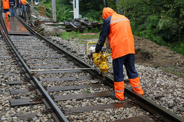 Worker repairs railroad on rainy day with machine