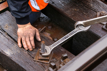 Worker tightens the screw on railroad with two spanners in hands