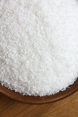 Dark wood bowl of dessicated coconut on wood table.