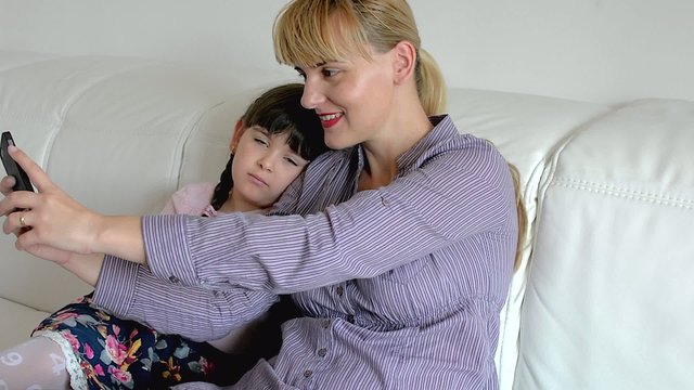 young mother and her daughter and take pictures on the sofa