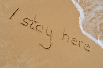 Text 'I stay here' in the sand