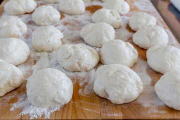 Small balls of fresh homemade dough on floured wooden board