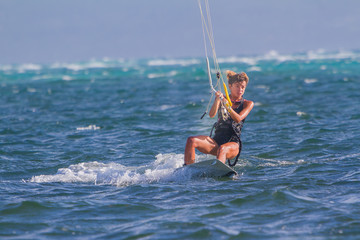A young woman kite-surfer rides in blue sea