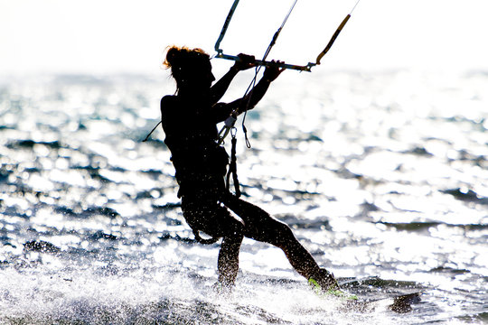 A young woman kite-surfer rides against the sun