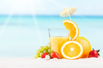     Fresh orange juice, fruits on sand with blue sky background