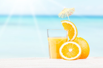     Fresh orange juice, fruits on sand with blue sky background