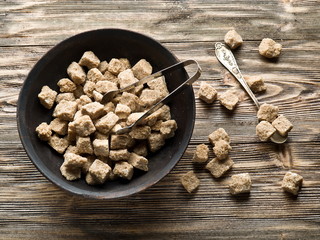 Cubes of cane sugar in the bowl on wooden table.