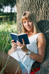 Fototapeta premium young woman sitting in the park and reading a book