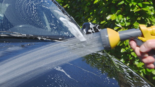 Car Care - Man using a garden spray gun to remove the soap