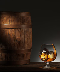 Glass of matured whiskey and old wooden barrel.