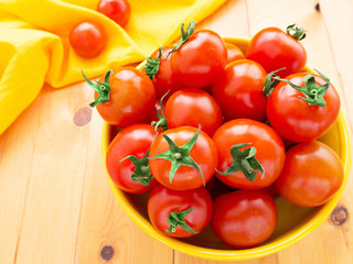Cherry tomatoes in the yellow bowl on the wooden background