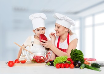 Adorable. Mother feeding kid daughter vegetables in kitchen