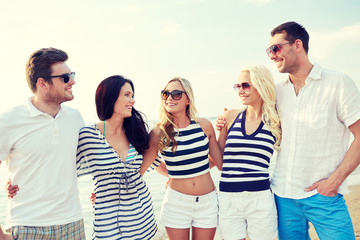 smiling friends in sunglasses talking on beach