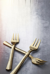 Old and Tarnished Gold Forks on textured background .