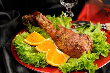 Roasted turkey drumstick with orange and lettuce on black and re