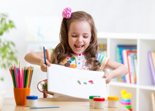 child girl painting and showing painting in nursery