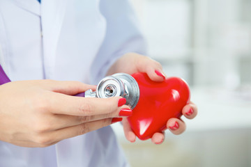 Young woman doctor holding a red heart, isolated on white