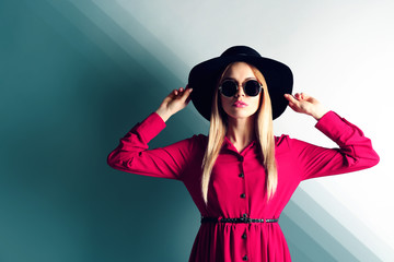 Expressive young model with hat and sunglasses on wall background