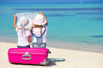 Little girls with big suitcase and map at tropical beach