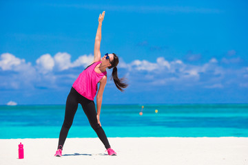 Fit young woman doing exercises on tropical white beach in her